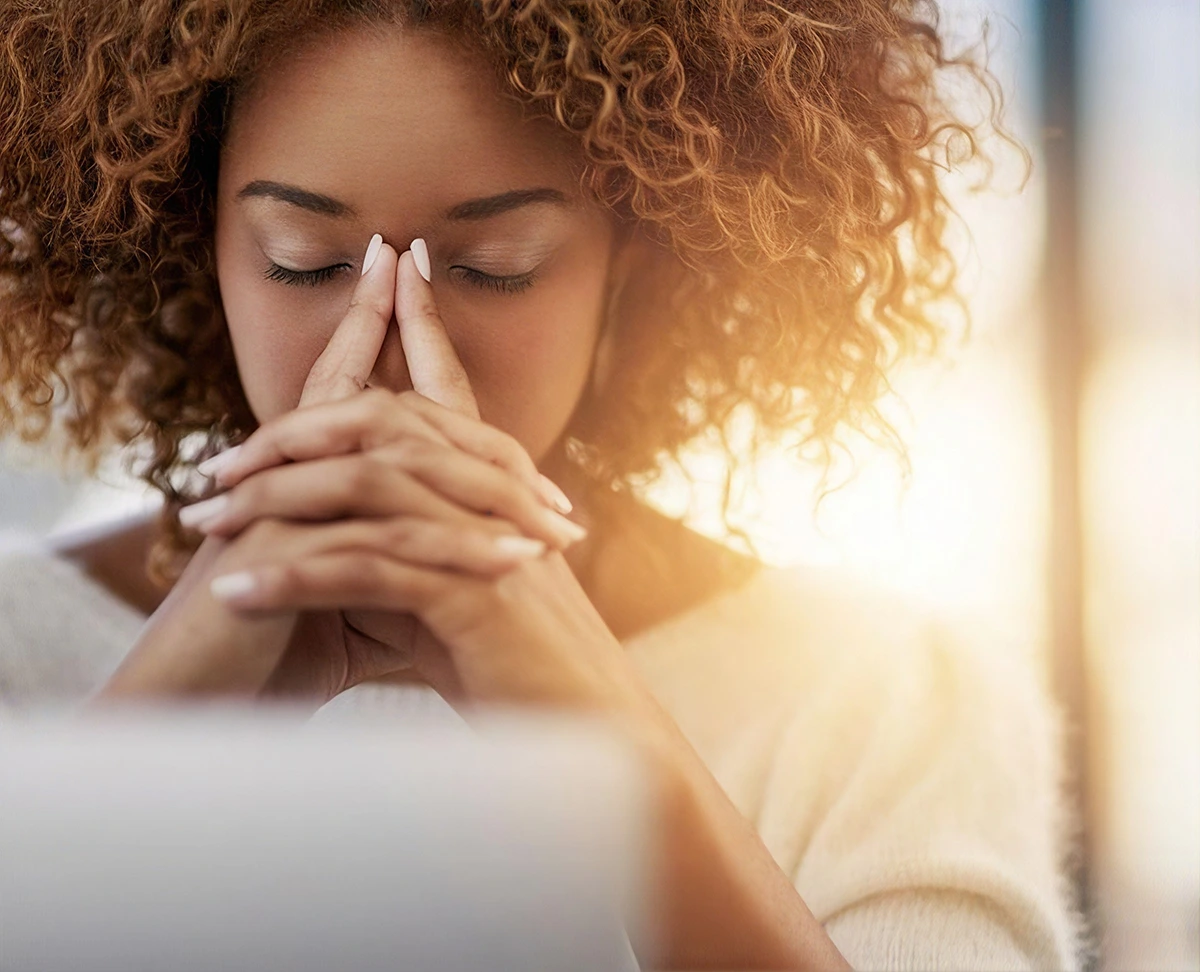 Woman with curly hair resting her hands against her face